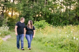 couple walking in field holding hands in the engagement portrait session