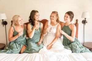 bride and bridesmaids on bed with champaign at Strathmere wedding in "the corner" rooms